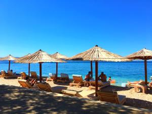 eine Gruppe von Menschen, die am Strand mit Sonnenschirmen sitzen in der Unterkunft Kristian Apartments in Podstrana