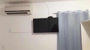 une télévision sur un mur à côté d'un rideau dans l'établissement Linhare's Suítes, aptos com e sem cozinha, à Búzios