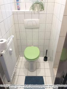 a green toilet in a white tiled bathroom at Schöne‘s Eck in Großröhrsdorf