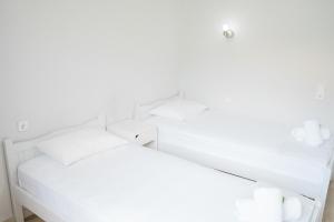 two white beds in a room with white walls at Afroditi Pansion in Agios Nikitas
