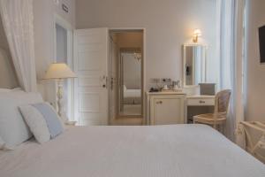 a white bedroom with a bed and a desk and a bathroom at Micra Anglia Boutique Hotel & Spa in Andros