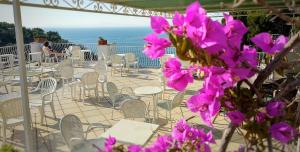 eine Terrasse mit Tischen, Stühlen und lila Blumen in der Unterkunft Hotel Desiree in Sorrent