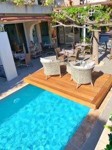 a pool with a wooden deck and chairs and tables at Hôtel Beau Soleil in Le Lavandou