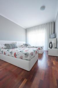 a white bedroom with two beds and a wooden floor at Apartamento Mouzinho de Albuquerque in Matosinhos