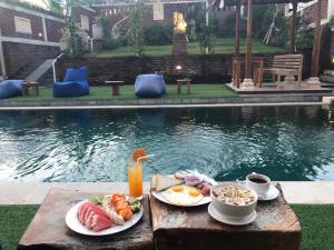a breakfast of eggs and fruit on a table next to a pool at Oka's Guest House Canggu in Canggu