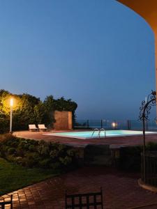 una piscina por la noche con dos bancos en B&B Villa Etelka, en Aci Castello