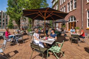 eine Gruppe von Menschen, die unter einem Schirm an Tischen sitzen in der Unterkunft Stayokay Hostel Amsterdam Oost in Amsterdam