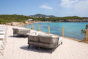 
a beach with chairs, a bench and a sailboat at BLESS Hotel Ibiza - The Leading Hotels of The World in Es Cana
