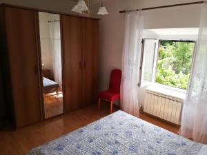 um quarto com uma cama, uma janela e uma cadeira vermelha em Apartment Luka em Mali Lošinj