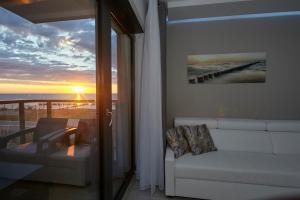 a living room with a couch and a balcony with a sunset at Gardenia Sea Side MARTINA 1 Dziwnów in Dziwnów