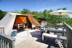 una terraza con una tienda, una mesa y una sombrilla en Ingerichte tenten Domaine les Gonies, en Mauroux