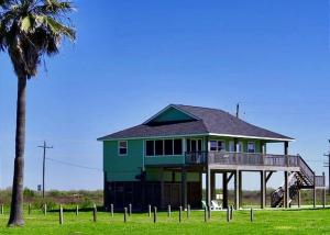 a green house with a deck and a palm tree at Mi Casa Del Mar Home in Caplen
