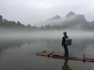 a man standing on a dock in the water at Yangshuo Yunshe Mountain Guesthouse in Yangshuo