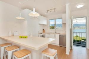 a white kitchen with a large island with stools at Monaco Waterside Magic in Nelson