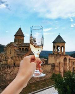 una persona sosteniendo una copa de vino frente a un castillo en Guest House Sveti en Mtskheta