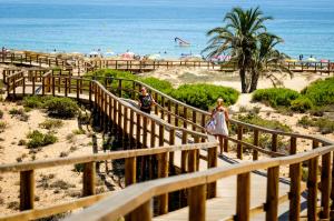 een man en vrouw die via een houten trap naar het strand lopen bij LightHouse View I in Gran Alacant