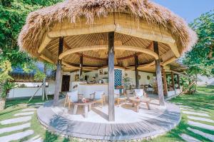 a pavilion with tables and chairs under a straw umbrella at Mule Malu Tropical Stay in Uluwatu