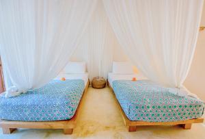 two beds in a room with white curtains at Mule Malu Tropical Stay in Uluwatu