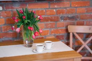 a vase of tulips and two cups on a table at Apartamenty Pocztowa in Bydgoszcz