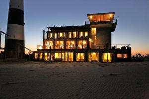 a building on the beach with a lighthouse in the background at Pelican Point Lodge in Walvis Bay