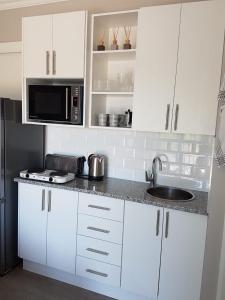 a kitchen with white cabinets and a sink and a microwave at Aloe @ the Sea in Mossel Bay