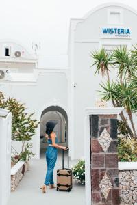 Eine Frau mit einem Koffer vor einem Gebäude in der Unterkunft Wisteria Apartments in Karterados