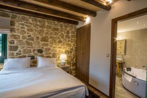 1 dormitorio con pared de piedra, 1 cama y bañera en Hotel Arhontiko Vourloka en Pramanta