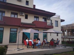 persone sedute ai tavoli con ombrelloni di fronte a un edificio di Stella Maris a Techirghiol