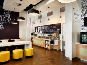 a restaurant with yellow stools and a kitchen with a counter at ibis Budget Auckland Airport in Auckland