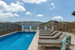 a swimming pool with chaise lounges and a rock wall at Mykonos Panormos Villas in Mykonos