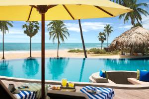 a pool with chairs and an umbrella and the ocean at Jetwing Surf & Safari, A Luxury Reserve in Arugam Bay