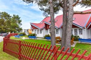 a red fence in front of a house with trees at Kotedžiukai Šventojoje in Šventoji