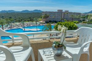 um pátio com cadeiras brancas, uma mesa e uma piscina em Hotel Club Cala Romani em Calas de Mallorca