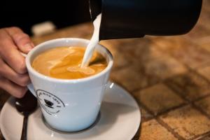 una persona está vertiendo leche en una taza de café en Dragonfly Hotel King's Lynn, en Kings Lynn