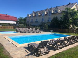 a swimming pool with chairs and a house in the background at Pensjonat Zenit in Ustronie Morskie