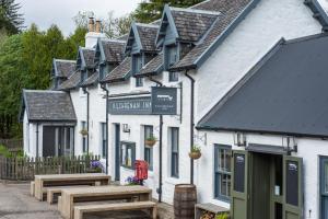 eine Reihe weißer Gebäude mit Holzbänken davor in der Unterkunft The Kilchrenan Inn in Oban