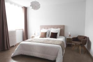 ein weißes Schlafzimmer mit einem großen Bett und einem Stuhl in der Unterkunft Au chalet des quatre saisons in Ax-les-Thermes