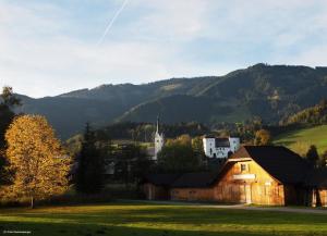 un fienile in un campo con una chiesa sullo sfondo di Biobergbauernhof Bergzeit Apartment in Goldegg a Goldegg