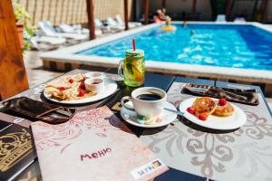 a table with plates of food and a cup of coffee next to a swimming pool at Hotel Seven in Lazarevskoye