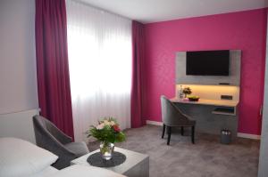 ein Hotelzimmer mit rosa Wänden und einem Schreibtisch mit einem TV in der Unterkunft Hotel Garni Nordseejuwel in Horumersiel