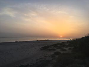 um pôr-do-sol numa praia com pessoas nela em ONUBA golf, sea & sun em El Portil