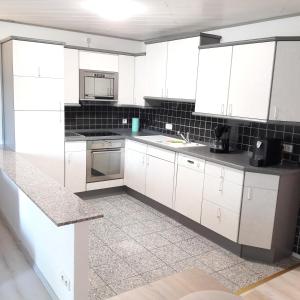 una cocina blanca con armarios y electrodomésticos blancos en holydayhome FeWo Schwarz, en Eberstadt