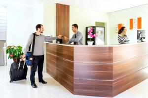 two men standing at a reception counter in a lobby at Hotel Stelati in Jaguariúna