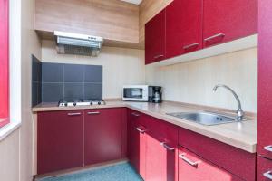 a kitchen with red cabinets and a sink at HH van Craenwick Appartement in De Hutte