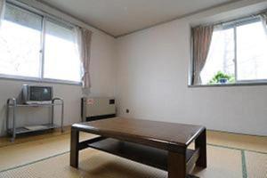 a living room with a coffee table and two windows at Kusatsu Kogen Youth Hostel in Kusatsu