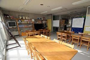 Kusatsu Kogen Youth Hostel في كوساتسو: فصل بطاولات وكراسي خشبية في فصل