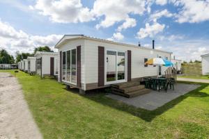 ein kleines weißes Haus mit einem Tisch und einem Sonnenschirm in der Unterkunft MB Noordiek Chalet in Hoek
