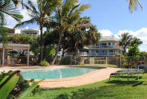 a swimming pool in front of a house with palm trees at Surfside On The Beach in Buddina