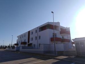 a white building with red balconies in a parking lot at Holly apartman in Umag