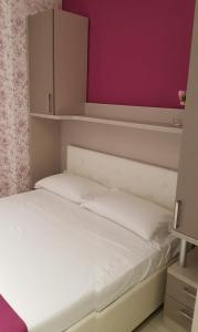 - une chambre avec un lit blanc et un mur rose dans l'établissement Eden Room, à Margherita di Savoia